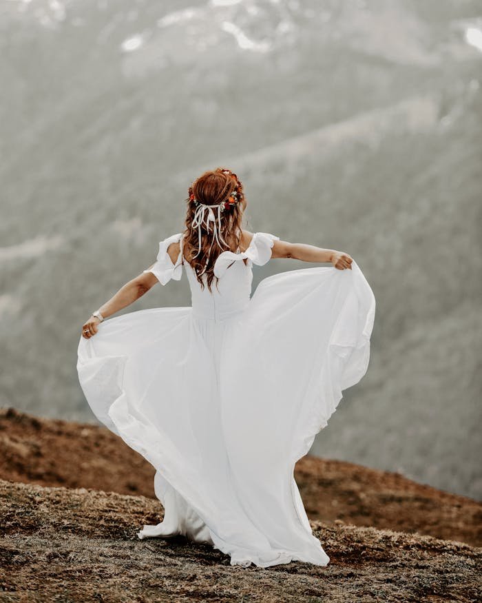 Back-view Photo of Woman in White Dress Standing on Brown Field